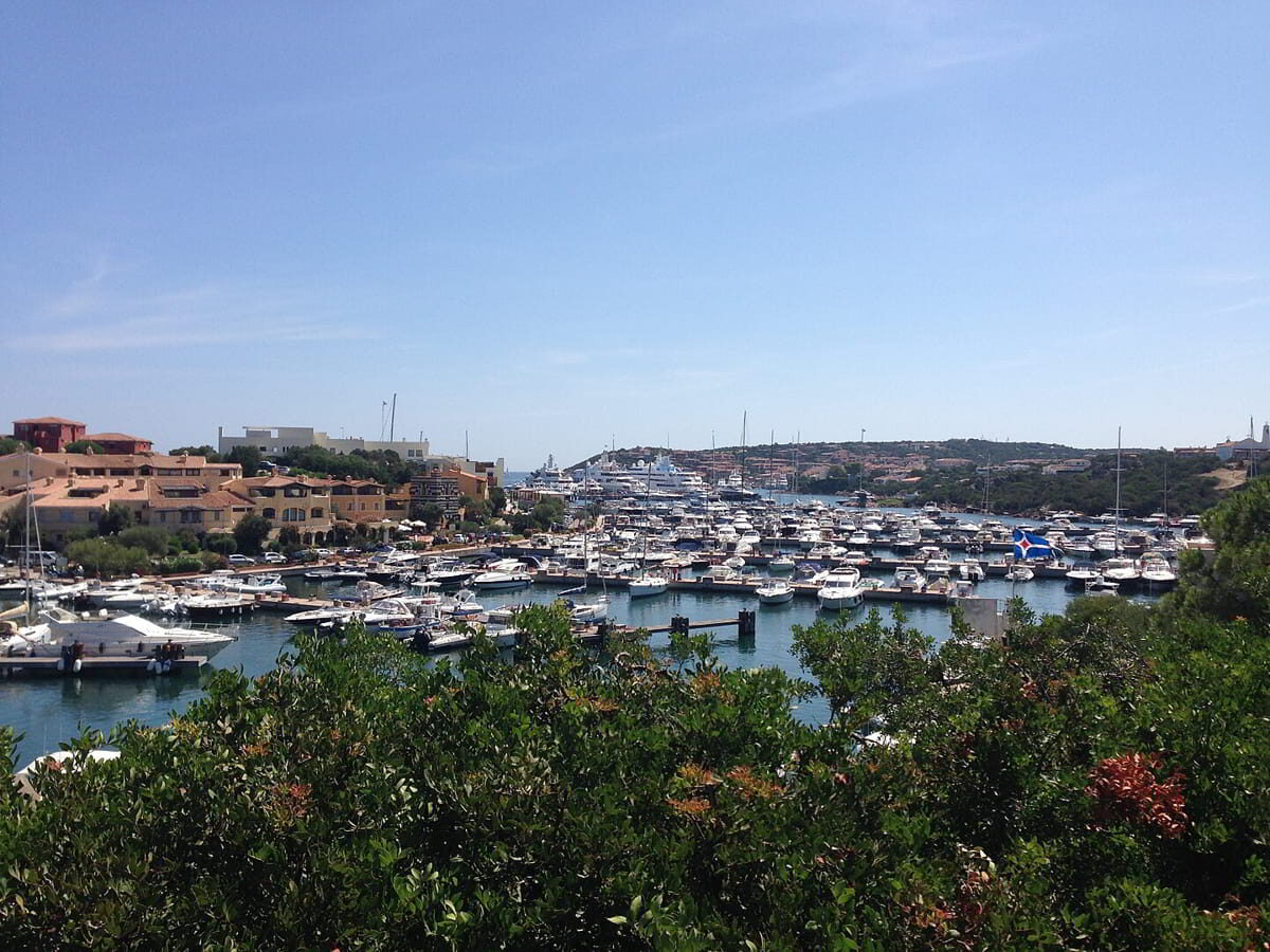 Daytime harbor view of Porto Cervo marina, showing yacht berths and coastal architecture in the heart of Costa Smeralda