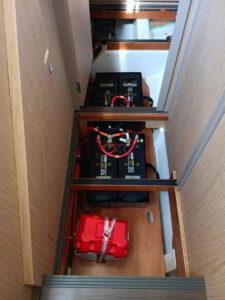 Yacht battery setup with technician checking cables and housing in engine room