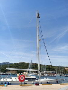 Technicians installing sailboat mast in Porto Cervo marina under sunny sky