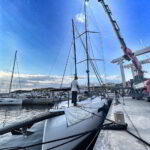 Technicians installing sailboat mast with crane in Porto Cervo marina under sunny sky
