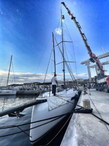 Technicians installing sailboat mast with crane in Porto Cervo marina under sunny sky